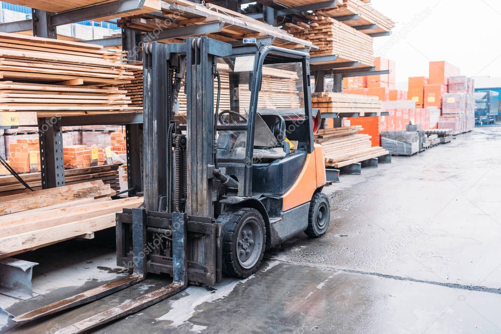 forklift machine standing at wooden planks on shelves outside