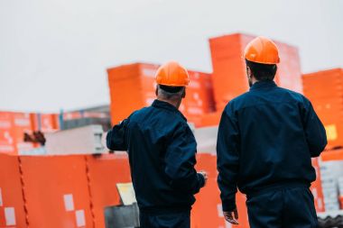 back view of two builders in helmets working outside on construction clipart