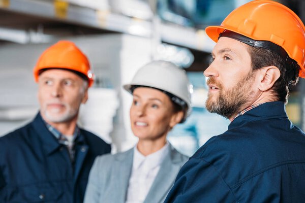 male workers and female inspector in helmets in storehouse