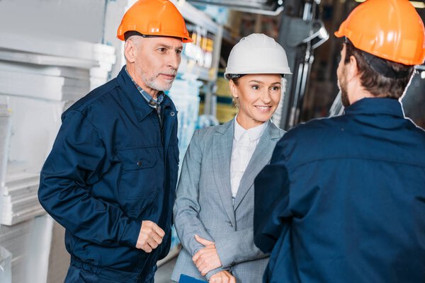 male workers and female inspector in helmets in storehouse