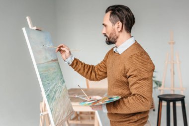sakallı adam sanat sınıfı şövale üzerinde boyama yan görünüm