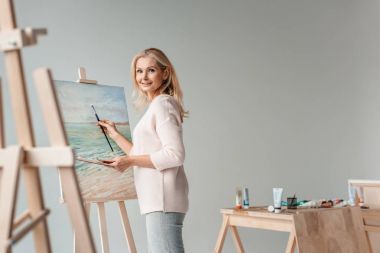 Fotoğraf art Studio şövale üzerinde resim yaparken gülümseyen Olgun kadın sanatçı
