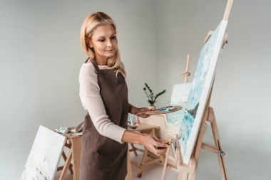 beautiful mature woman in apron painting on easel at art class  clipart