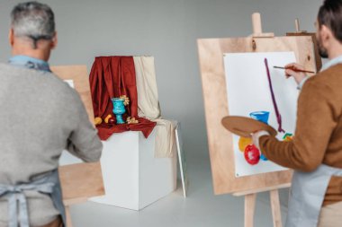 back view of two men painting still life on easels at art class clipart