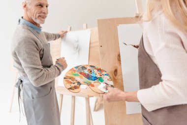 cropped shot of senior people painting on easels at art class clipart