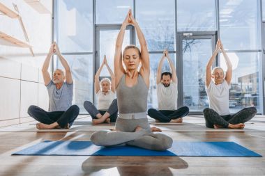 group of senior people practicing yoga with instructor in lotus pose on mats in studio clipart