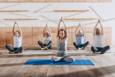 group of senior people practicing yoga with instructor in lotus pose on mats in studio clipart