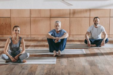 yoga paspaslar üzerine oturan ve kameraya gülümseyen olgun erkek ile kadın öğretim üyesi