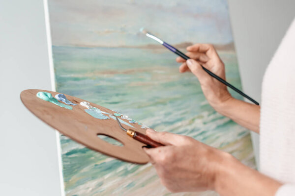 обрезанный снимок художника, держащего палитру и кисть во время рисования в мольберте в художественной студии
 