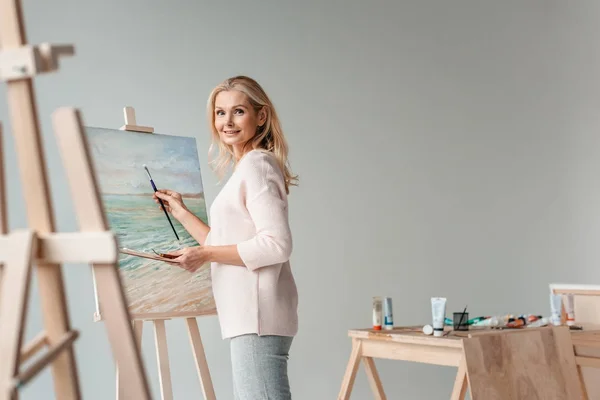 Artista Femenina Madura Sonriendo Cámara Mientras Pinta Caballete Estudio Arte — Foto de Stock