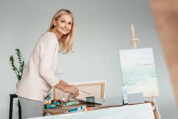Schöne Reife Frau Lächelt Die Kamera Während Sie Kunstwerkzeuge Kunstatelier — kostenloses Stockfoto