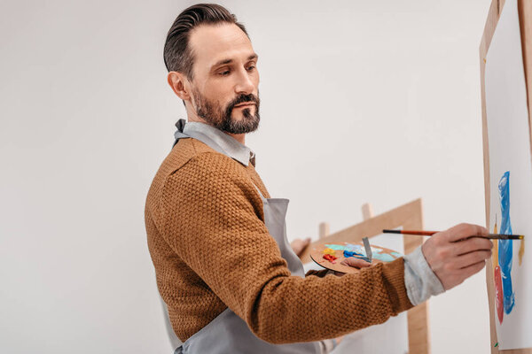 mature male artist holding palette and painting in art studio