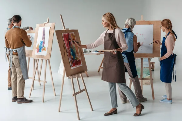 Grupo Estudiantes Adultos Masculinos Femeninos Delantales Pintando Juntos Caballetes Clase — Foto de Stock