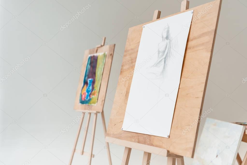easels with artistic paintings in empty art studio on grey