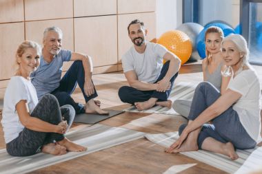 Olgun insanlar yoga paspaslar üzerine oturan ve kameraya bakarak eğitmen ile
