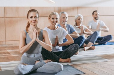 senior people with instructor sitting in lotus position on yoga mats  clipart