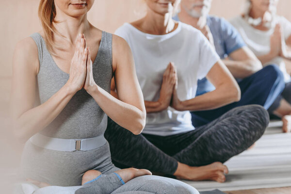 cropped shot of senior people with instructor sitting in lotus position on yoga mats