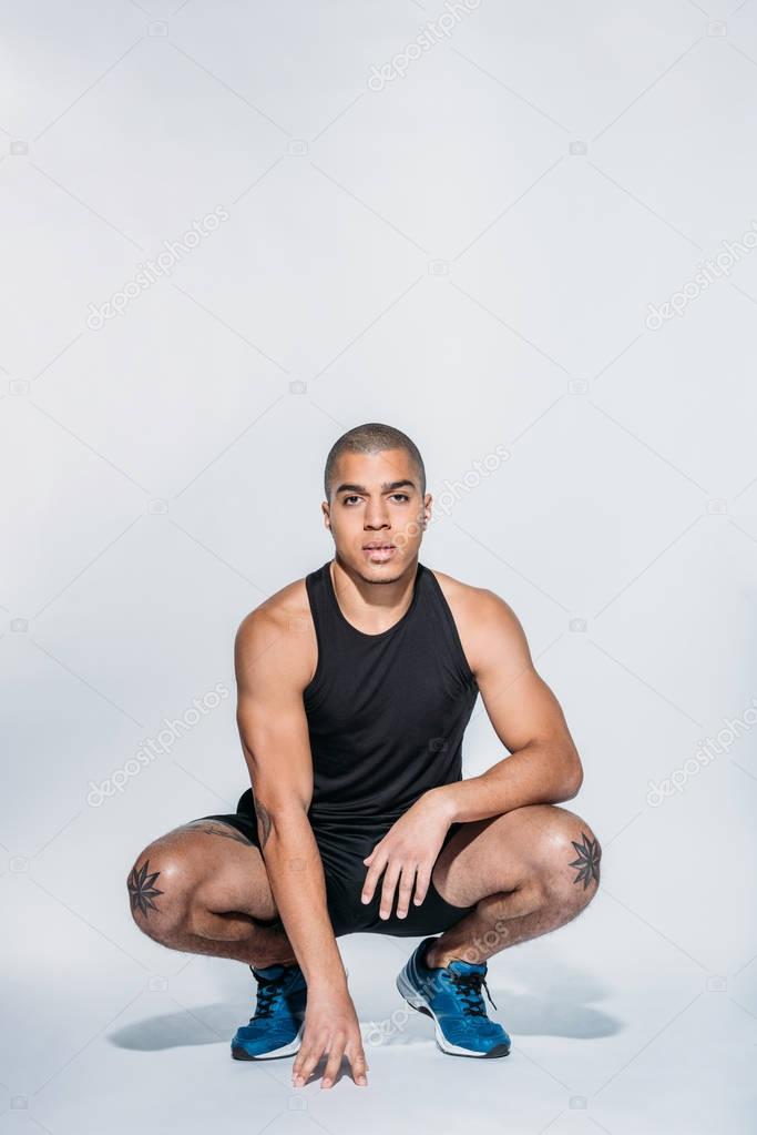 sportive african american squatting and looking at camera