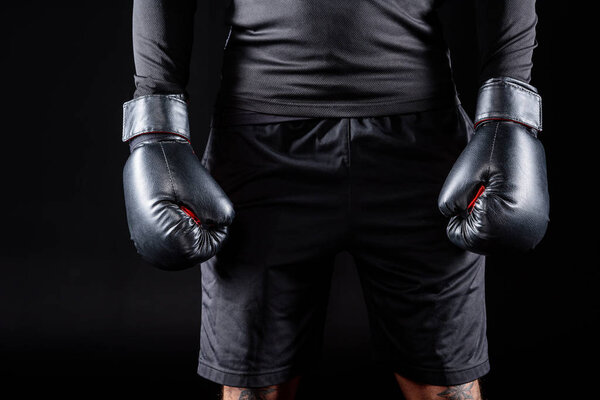 cropped shot of boxer in black gloves isolated on black