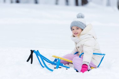 seçici odak bir kızak parkta oturan gülümseyen çocuk