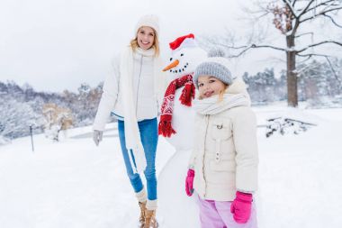 mutlu anne ve kızı kamera ile kış Park kardan adam dururken gülümseyen