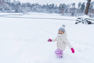 Karda oynarken ve kış park kamerada gülümseyen güzel mutlu çocuk 