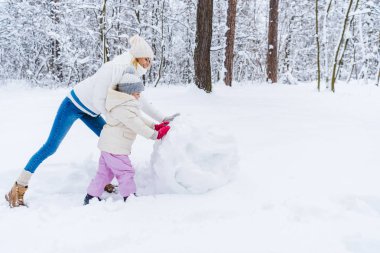 mutlu anne ve kızı kış parkta kardan adam yapma yan görünüm