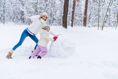 mutlu anne ve kardan adam yapma ve kış park kamerada gülümseyen kız