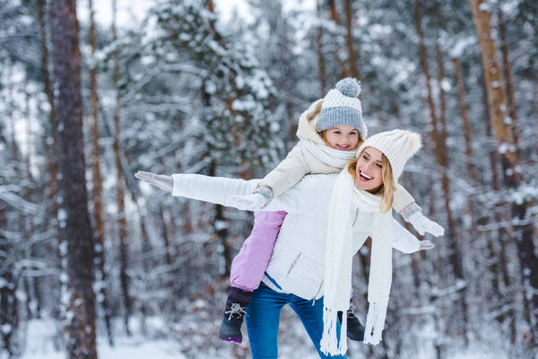 cheerful mother and little kid piggybacking together in winter park