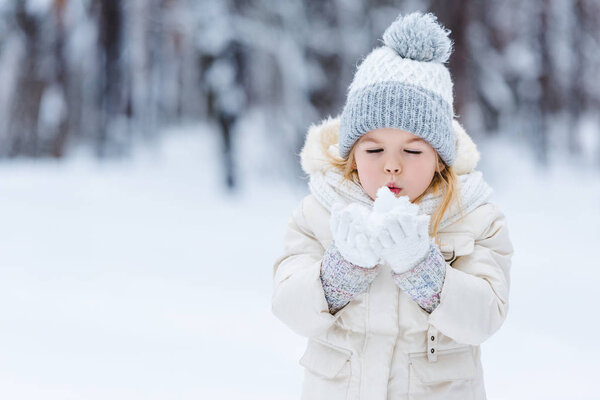 portrait of adorable kid blowing onto snow ball in hands in winter park