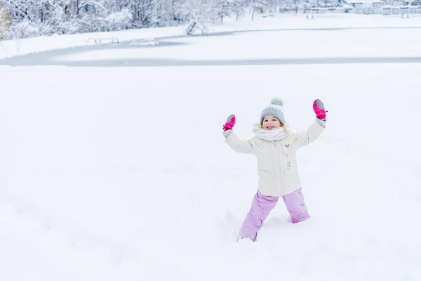 Очаровательный Счастливый Ребенок Поднятыми Руками Варежках Стоящих Снегу Улыбающихся Камеру — Бесплатное стоковое фото