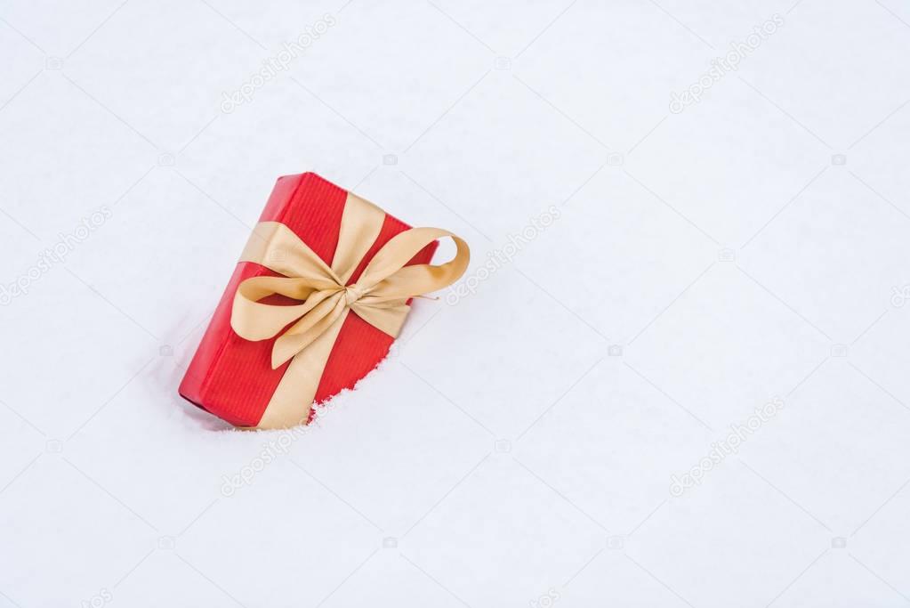 close-up view of red gift box with golden ribbon in snow 
