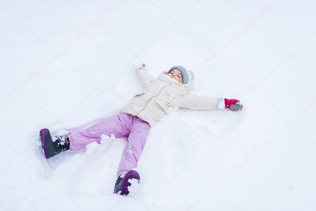 cute little child in warm clothes making snow angle