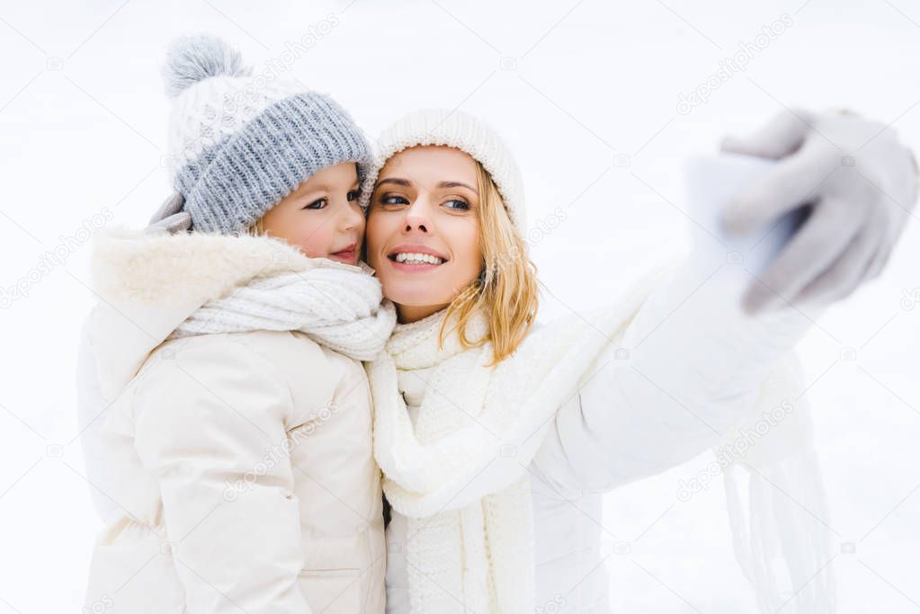 happy mother and daughter taking selfie in winter park