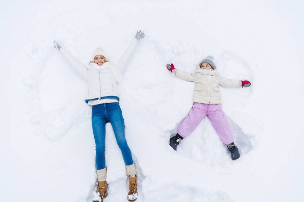 top view of happy mother and daughter making snow angels together 
