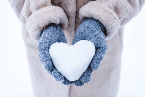 обрезанный снимок человека, держащего символ сердца, сделанный из снега
