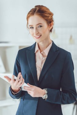 Tablet tutarak ve kameraya bakarak gülümseyen iş kadını