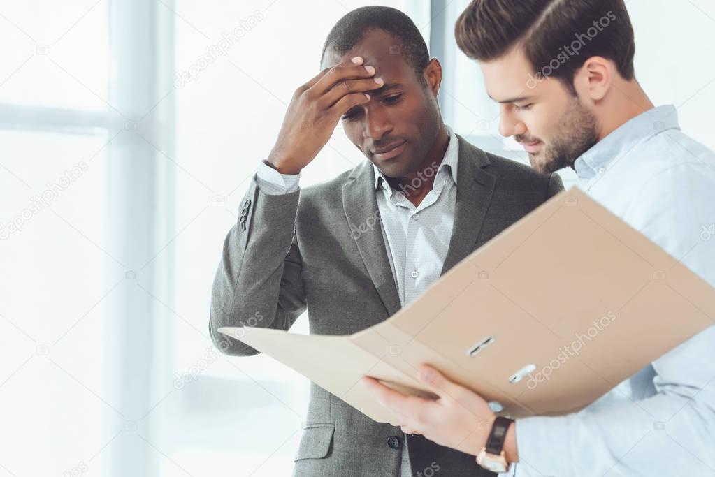 african american and caucasian businessmen looking at documents in folder