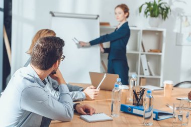 Masada oturan ve ofis alanı, flipchart işaret eden kadın isteyen iş adamları
