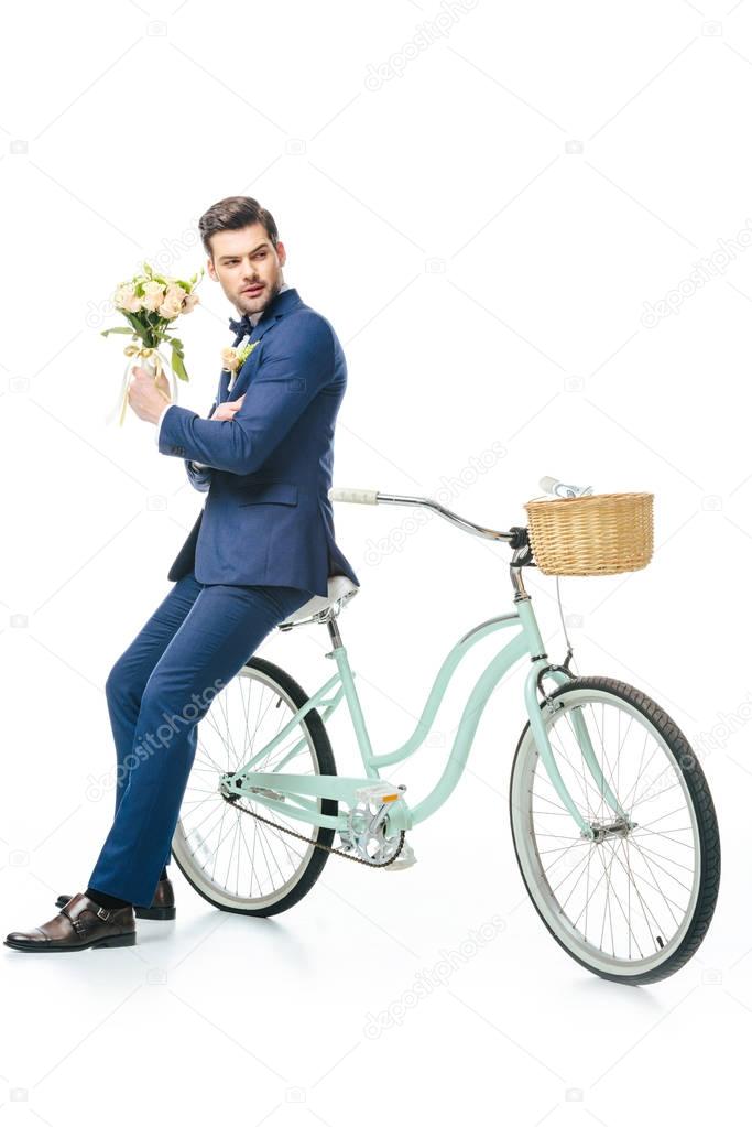 stylish groom with wedding bouquet leaning on retro bicycle isolated on white