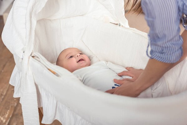 partial view of baby in crib and mother standing near by at home