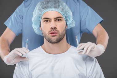 shocked handsome man in medical cap making beauty injections, isolated on grey clipart