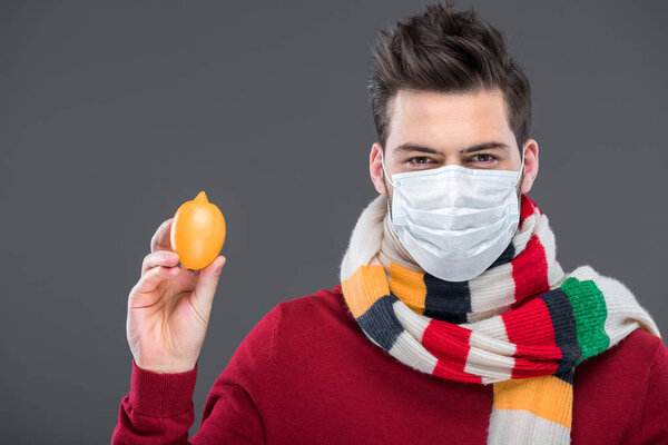sick man in warm scarf and medical mask holding lemon, isolated on grey