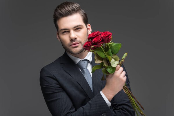 handsome man in suit holding bouquet of red roses, isolated on grey