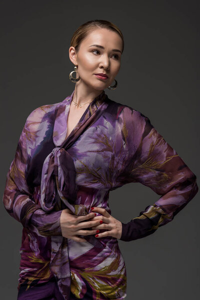 portrait of elegant kazakh woman posing with hands on waist and looking away isolated on grey