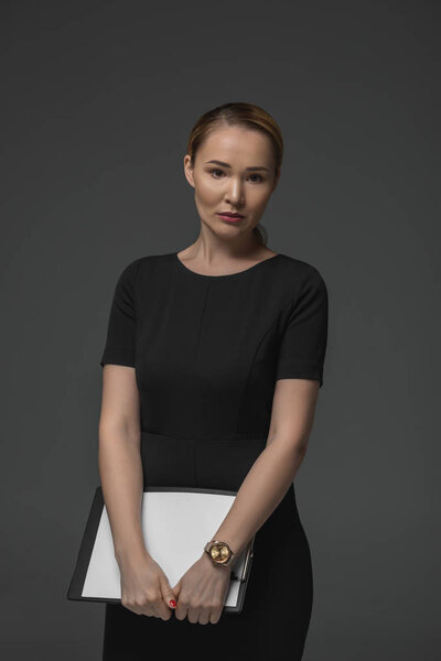 beautiful kazakh businesswoman holding clipboard and looking at camera isolated on grey 