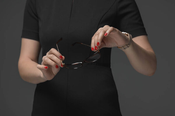 cropped shot of woman holding eyeglasses and checking wristwatch isolated on grey