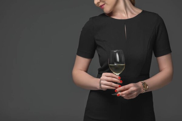 cropped shot of elegant woman in black dress holding glass of wine isolated on grey