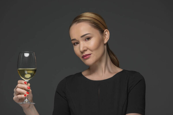 smiling kazakh woman holding glass of wine and looking at camera isolated on grey