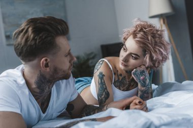 birbirine bakarak ve yatak yatak odasında yatan genç dövmeli aşıklar